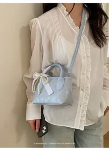 Dettaglio borsa a secchiello azzurra con fiocco bianco e ciondolo con perle