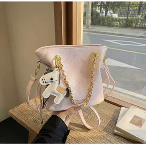 Detail of pink quilted bucket bag with gold chain and horse charm on wooden table