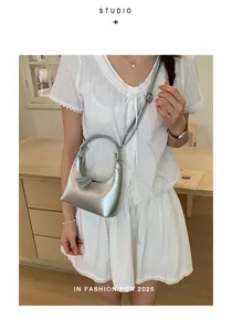 Silberne Metallic-Halbmondtasche mit rundem Metallgriff und Quaste am Modell gezeigt