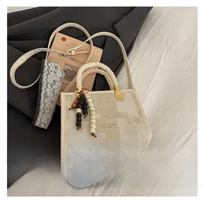 Détail d'un sac carré beige avec poignée tressée et accessoire de breloque en perles