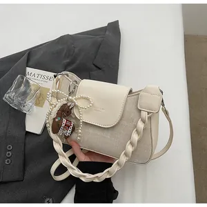 Detailed close-up of ivory crossbody bag with woven leather strap and pearl charm