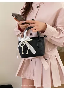 Dettaglio di piccola borsa nera con fiocco bianco e ciondolo di perle eleganti
