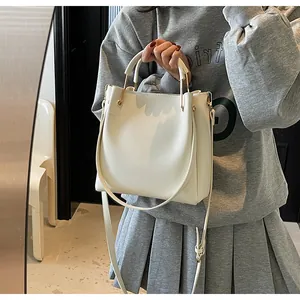 Dettaglio di una borsa a secchiello bianca minimalista con finiture in oro e manici