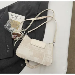 Detail of beige textured handbag featuring pearl chain and horse charm on grey background