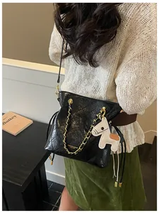 Detail of black quilted bucket bag with gold chain and white horse charm on a model
