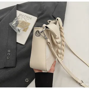 Detail of a creamy white leather handbag with intricate braided handle and silver buckle