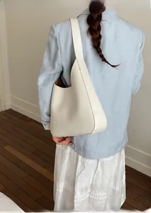 Close-up of minimalist cream-white leather bucket bag worn by model in a soft indoor setting