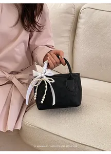 Dettaglio borsa nera in ecopelle con ciondoli di perle eleganti e fiocco in seta bianca