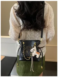 Detail of black quilted bucket bag with gold chain and horse charm on a model