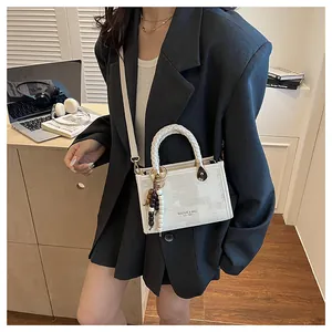 Détail du sac blanc avec poignée tressée et perles en bois sur un blazer noir