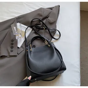 Dettagli della borsa a secchiello nera con borchie dorate e tracolla su blazer grigio