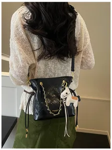 Detail of a black quilted chain bucket bag with a white horse charm worn by a model