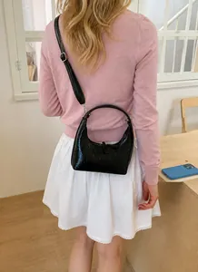 Detail einer schwarzen Halbmond-Tasche mit Faltenstruktur, getragen von einem Model im Licht