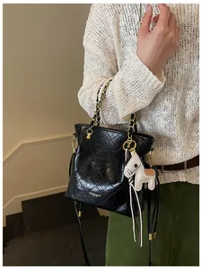 Detail of black quilted chain bag with gold logo and white pony charm on a model
