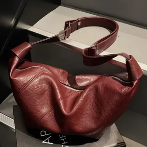Borsa a bignè in pelle rosso scuro con tracolla larga su sfondo minimalista moderno