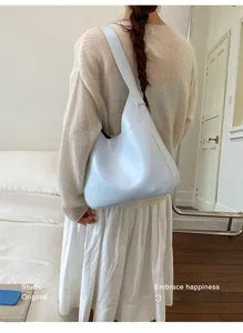 Close-up of a minimalist light blue hobo bag with a wide strap on a model's shoulder