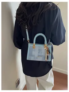 Détail du sac bandoulière bleu clair avec texte doré et pendentif décoratif en perles