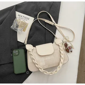 Detail of cream crossbody bag featuring a thick braided handle and a cute horse charm