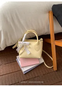 Dettaglio mini borsa giallo crema con fiocco di seta e ciondolo di perle su libri