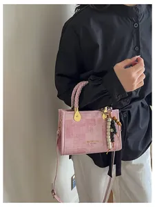 Détail d'un sac bandoulière rose avec poignée tressée, logo doré et pendentif en perles