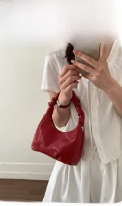Macro detail of red ruched shoulder bag with glossy PU texture and bow handle