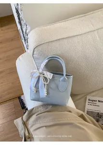 Mini borsa a mano celeste con fiocco di perle su un divano in tessuto color crema