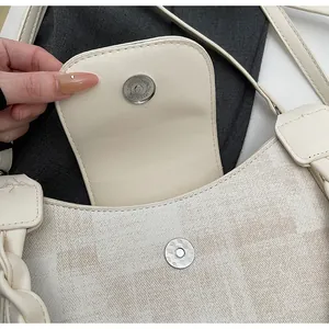 Close-up of magnetic buckle and woven handle detail on a beige plaid canvas bag