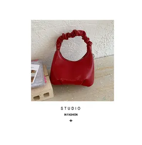 Macro detail of red ruched handle handbag with glossy leather finish in a studio setting