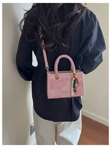Détail du sac bandoulière rose avec poignée tressée et breloque en perles colorées