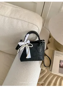Dettaglio della borsa a secchiello in pelle nera con fiocco in seta e perla