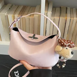 Rosa Lederhandtasche im Dumpling-Stil mit Silberverschluss und Plüschtier-Anhänger vor Bücherregal