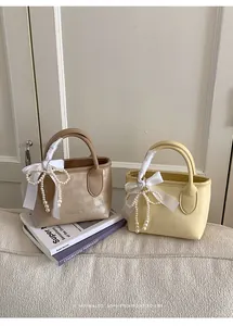 Dettaglio di mini borse con nastro bianco e ciondolo a fiocco di perle sul manico