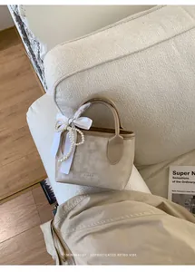Dettaglio della borsa beige con tracolla di perle e decorazione fiocco di raso