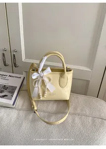 Dettaglio borsa a secchiello beige con ciondolo di perle e fiocco in seta bianca