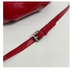Close-up of red glossy shoulder bag with adjustable strap and silver metal buckle detail