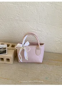 Dettaglio di borsa in pelle rosa chiaro con fiocco di perle e nastro di seta sul manico