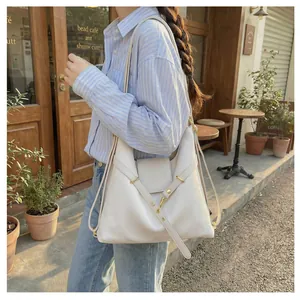 Detailopname van ivoorkleurige leren tas met metalen gespen en reliëflogo op de flap
