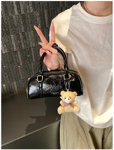 Detail of black glossy small cylinder handbag with golden hardware and plush bear charm