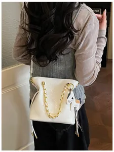 Detail of white quilted bucket bag with gold chain and horse charm on shoulder