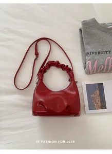Flat lay of red pleated handbag with rouching handle and adjustable strap over white fabric
