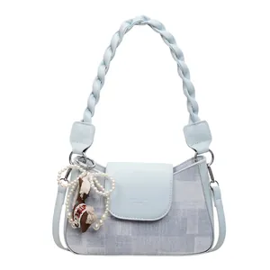 Light blue crescent handbag with braided handle and pearl bow charm on white background