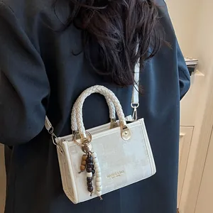 Sac cabas blanc en tissu texturé avec anses tressées et breloque porté par un mannequin