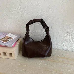 Detail of dark brown pleated hobo bag with scrunchie handle and polished leather texture