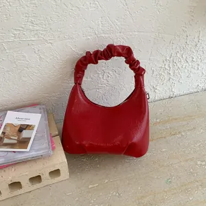 Detail view of red pleated handle handbag with elegant crescent shape and leather texture