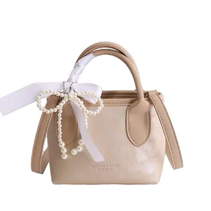 Elegante borsa a secchiello in pelle beige con ciondolo a perla e tracolla staccabile