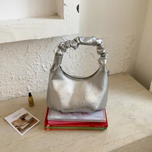 Close-up of metallic silver pleated handbag with ruched handle on decorative books