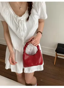 Close-up of a red pleated handbag with a crescent shape and glossy leather finish