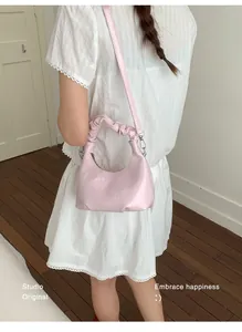 Detailed close-up of light pink glossy leather bag with embossed logo and pleated handle