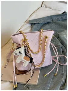 Detail of pink quilted bucket bag with gold chain strap and a horse charm on a bed