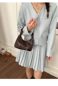 Detail of a dark brown oil-wax leather hobo bag with unique handle knot on blue blazer